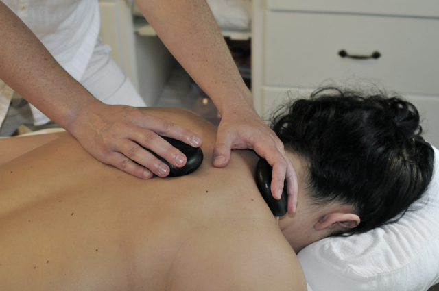 Emily Bilodeau administering a warm stone massage to clent's shoulder and neck